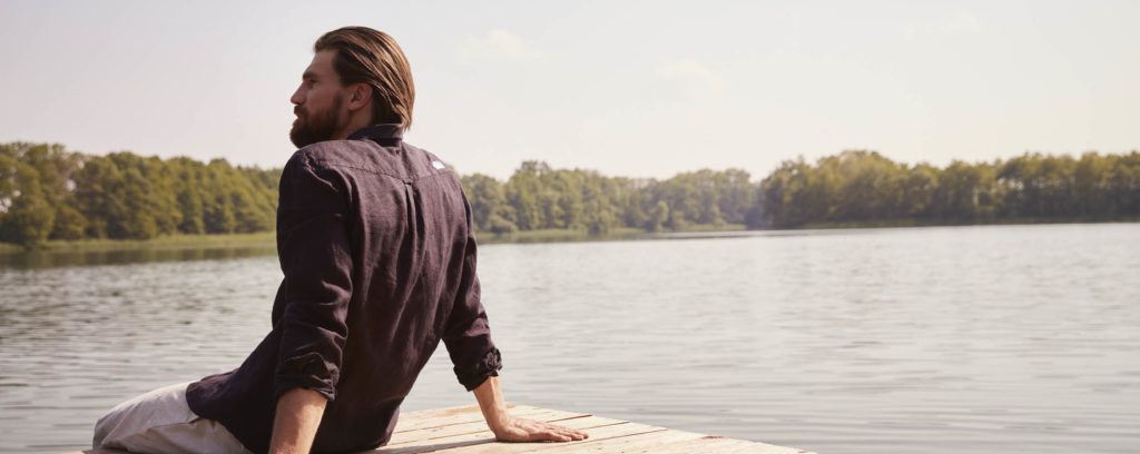 Back view of man sitting on edge of wooden jetty over a lake