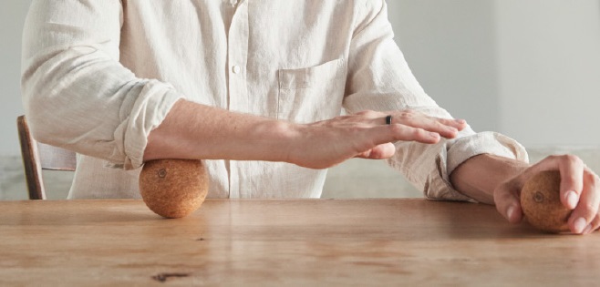 Man using a cork fascia ball to massage his forearm by rolling it between his arm and the table
