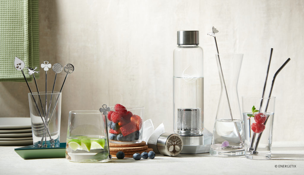 Table with various glasses and jugs, holding Magnetic Sticks and reusable stainless steel straws, next to a Balance Plus water bottle and magnetic coasters 