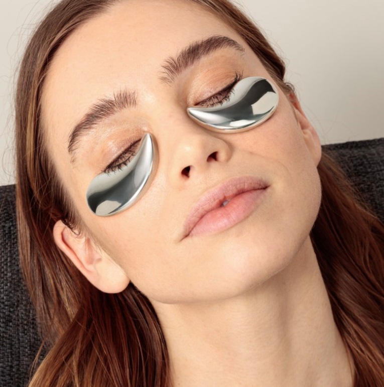 A person with their head back and eyes closed, with two Magnet Cool Eyes resting on their face under their eyes.