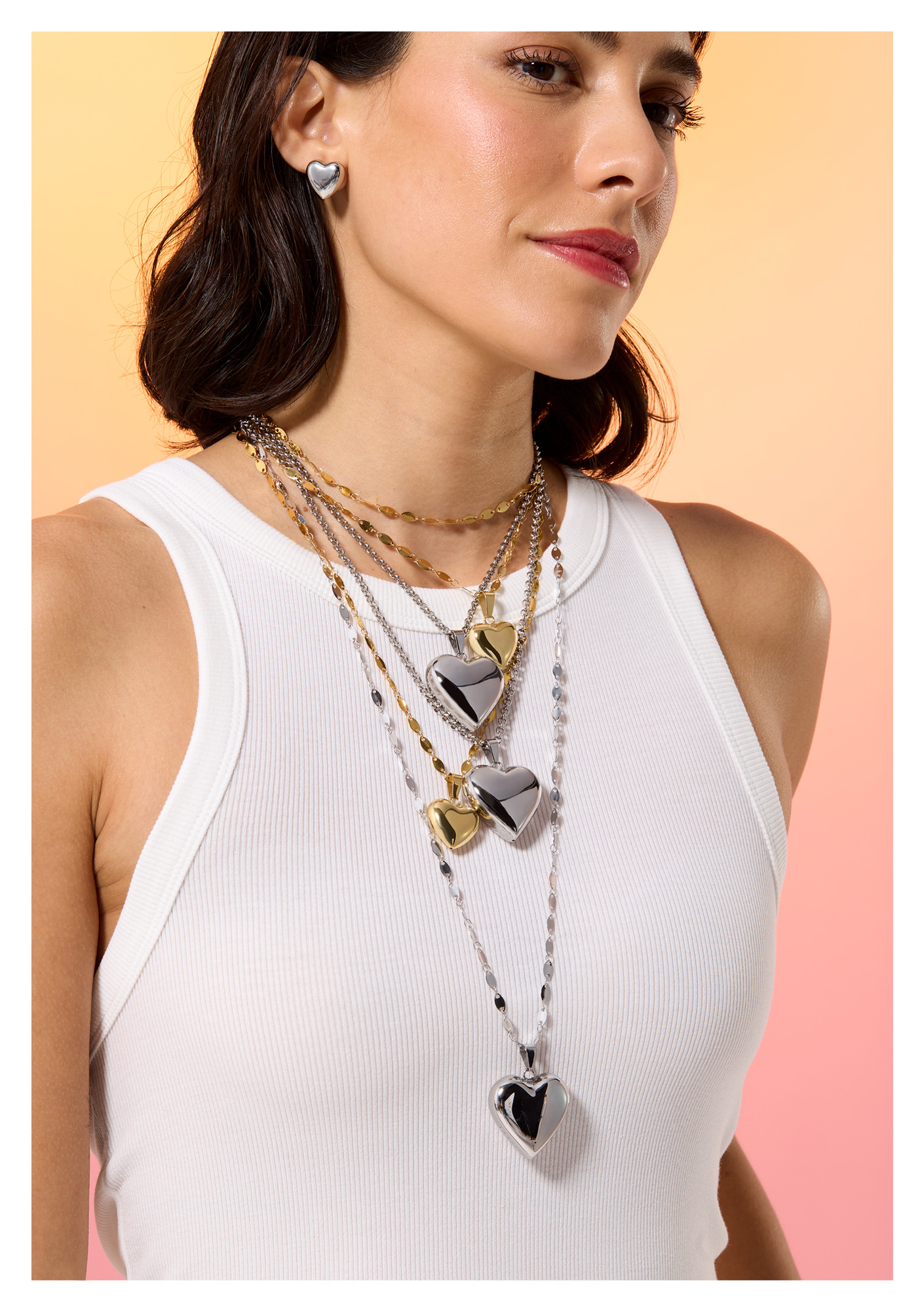 A model wearing five different gold and silver colour, large heart pendents, on different length chans. She also wears heart shaped ear studs.