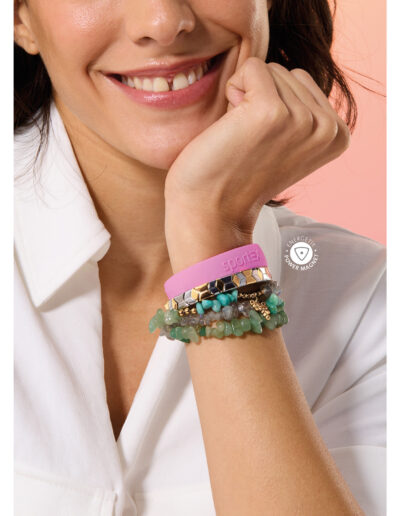 A smiling model resting her chin on her hand. She is wearing a pink colour sportEX bracelet, a silver and gold colour flexibracelet, and a mixed gemstone necklace that has been tripled wrapped around her wrist.