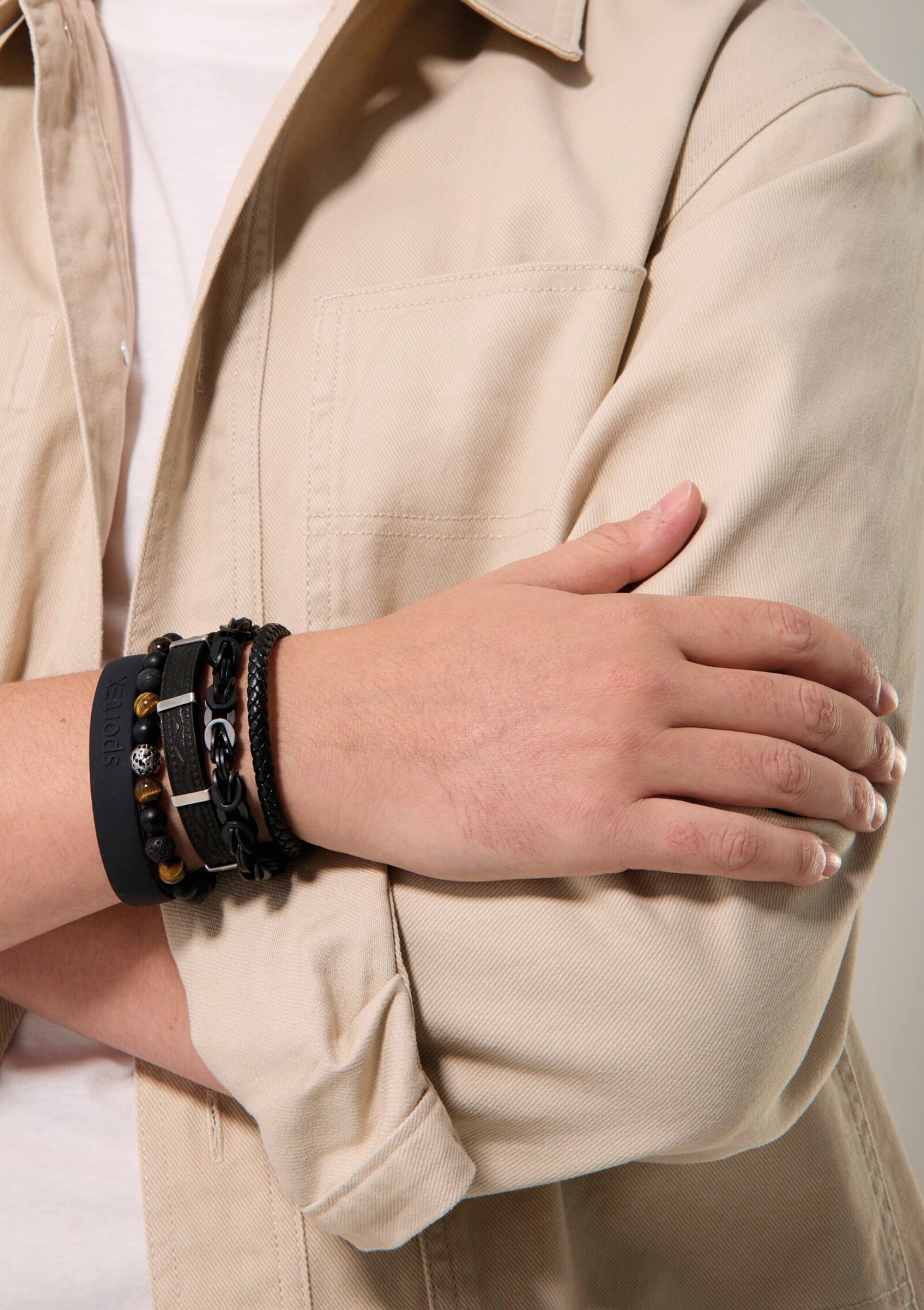 A mans torso with his arms across his chest. On his wrist are five different style magnetic bracelets in black, with materials of steel, leather, gemstones and silicone.